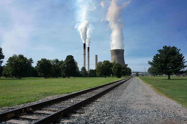 Railroad track to a coal-burning power plant with smoke stacks and a cooling tower