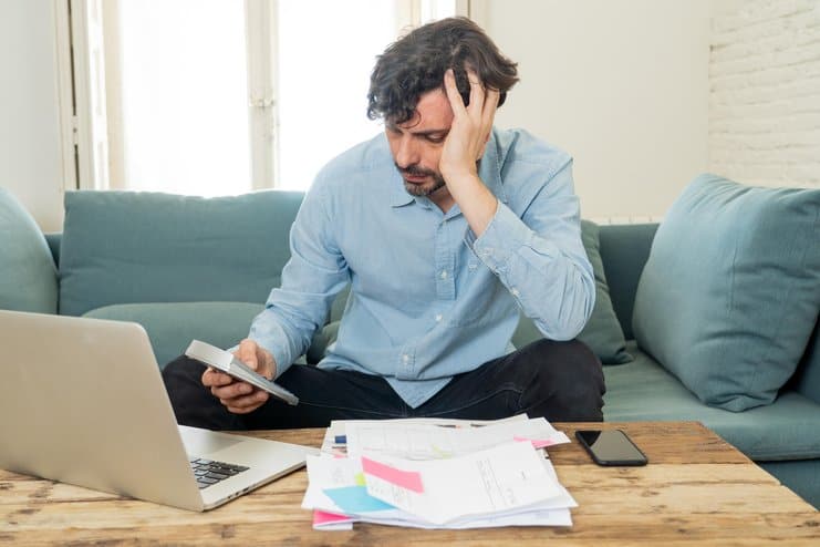 young angry and worried man working with laptop at home looking at bills and paying bills in home finance concept