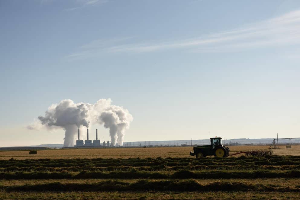 Emissions rising from a coal-fired power plant station smoke stacks with a tractor plowing a field in the foreground, near Wheatland, Wyoming.